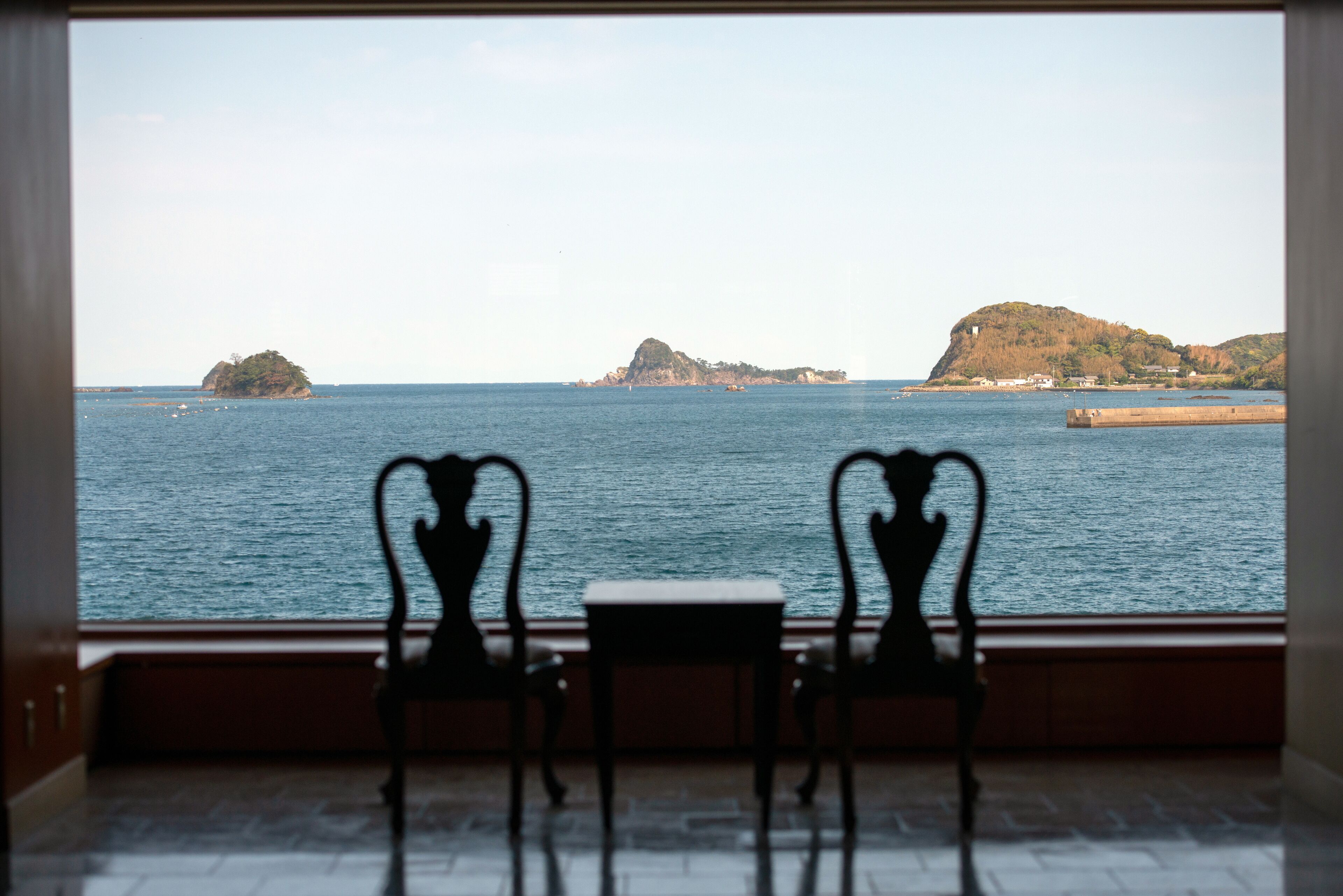 A view from a window with two chairs facing a body of water and distant islands.