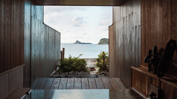Een houten interieur met uitzicht op een strand, een houten terras en een kleine tuin.