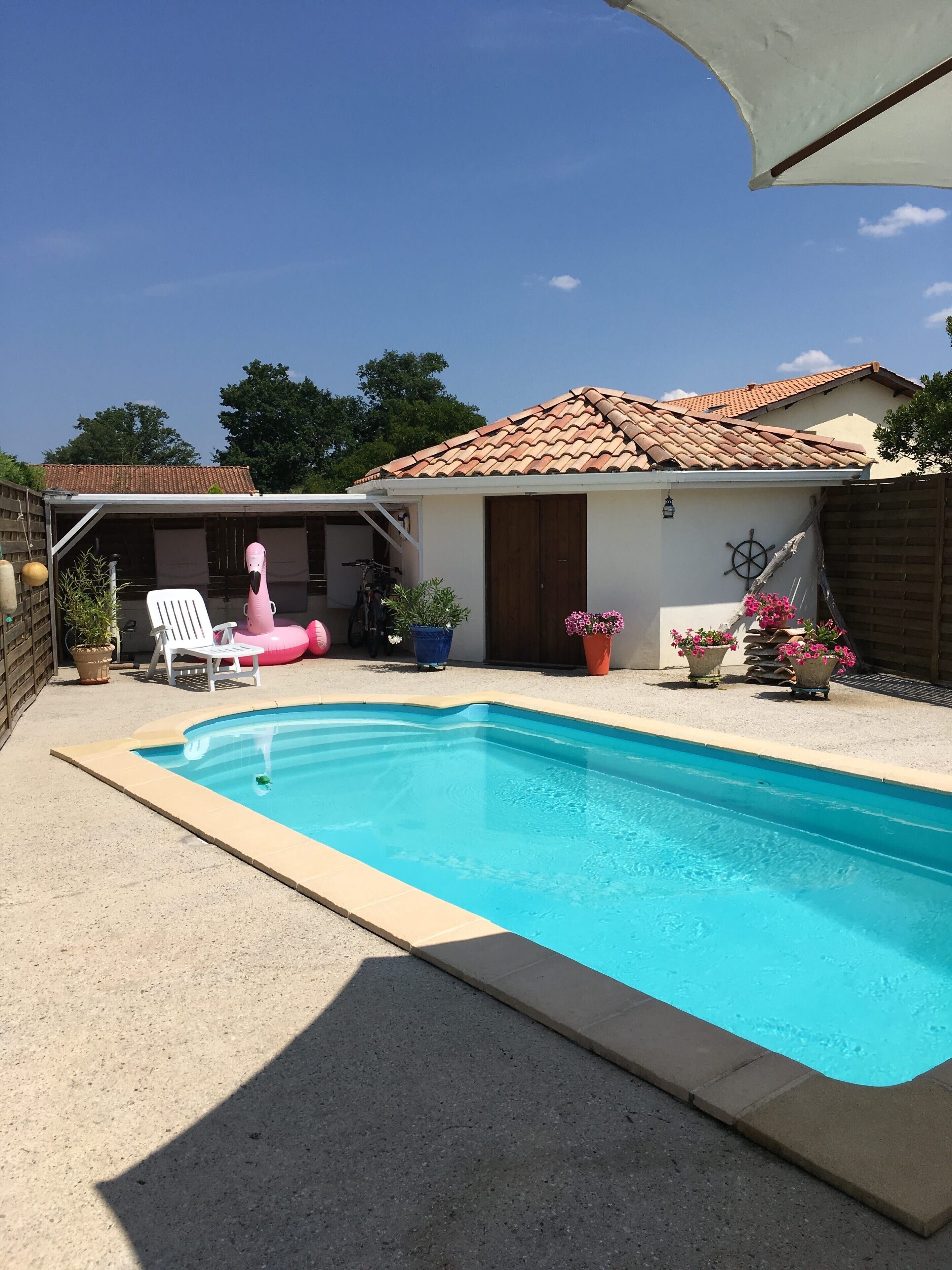 Uma piscina com deck ladrilhado, um espaço de varanda coberto e uma casa pequena com telhado telhado.