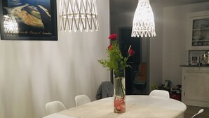 Ruokailutila, jossa on valkoinen pöytä ja tuolit, maljakko, jossa on punaisia kukkia, sekä kaksi riippuvalaisinta.