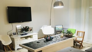 Moderni olohuone, jossa on litteänäyttöinen televisio, ruokapöytä, sohva ja nojatuoli.