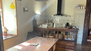 A kitchen with a wooden table, benches, and a hanging light fixture. - Authentic sheepfold renovated  (Sazos)