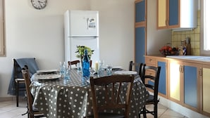 Un coin repas avec une nappe à pois, des chaises en bois, une horloge au mur et un réfrigérateur blanc.