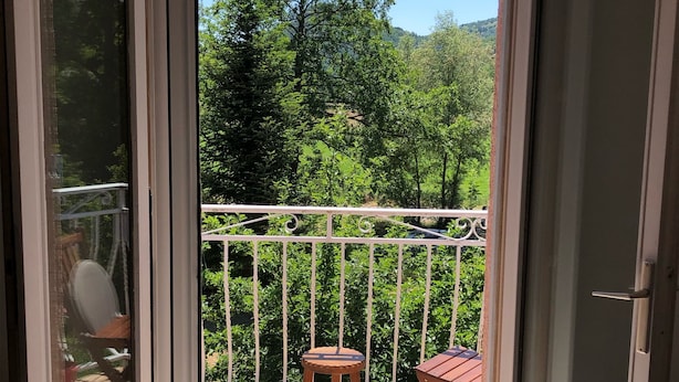 Un balcon donnant sur une zone boisée, avec une balustrade blanche et deux tabourets en bois.