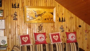 A cozy room with wooden paneling, a framed landscape painting, and decorative pillows with heart and deer motifs. - GITE upstairs in the owner's house (Haselbourg)
