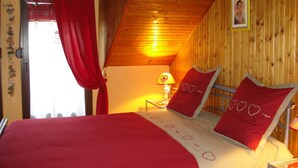 A cozy bedroom with a wooden ceiling, a bed with red bedding, a nightstand with a lamp, and a framed picture on the wall. - GITE upstairs in the owner's house (Haselbourg)