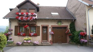 A two-story house with a brown door and windows, surrounded by flower boxes and greenery. - GITE upstairs in the owner's house (Haselbourg)