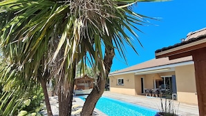 A pool area with a wooden deck, a palm tree, and a building with a tiled roof. - EXCEPTIONAL, PEACEFUL VILLA WITH HEATED POOL IN LÈGE CAP-FERRET (Lège-Cap-Ferret)