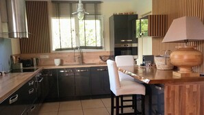 A modern kitchen with a central island, dark cabinetry, and a wooden accent wall. - EXCEPTIONAL, PEACEFUL VILLA WITH HEATED POOL IN LÈGE CAP-FERRET (Lège-Cap-Ferret)