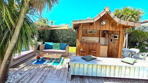 A wooden cabin with a deck, a small kitchen area, and a seating area with cushions. - EXCEPTIONAL, PEACEFUL VILLA WITH HEATED POOL IN LÈGE CAP-FERRET (Lège-Cap-Ferret)