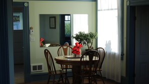 A dining area with a round table, six wooden chairs, and a potted plant with red flowers. - A View of the Strait of Juan de Fuca (Port Angeles)