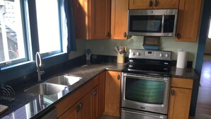 A kitchen with wooden cabinets, stainless steel appliances, a double sink, and a window with curtains. - A View of the Strait of Juan de Fuca (Port Angeles)