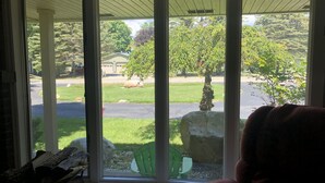 Une pièce dotée d’une grande fenêtre donnant sur un jardin avec une pelouse, des arbres et un bâtiment en arrière-plan.