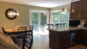 Une cuisine avec un coin repas, des meubles en bois, un îlot central intégré et une grande fenêtre offrant une vue sur l’extérieur.
