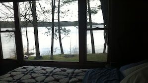 Een slaapkamer met een groot raam met uitzicht op een meer en bomen.