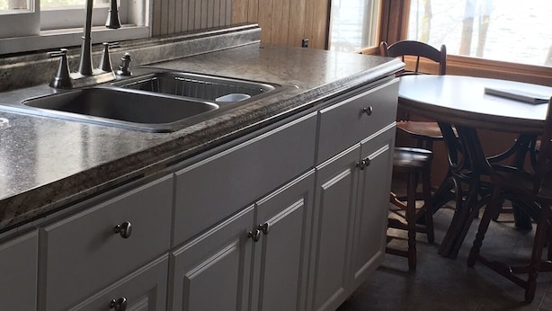 Een keuken met een dubbele spoelbak, witte kastjes en een eethoek met een tafel en stoelen.