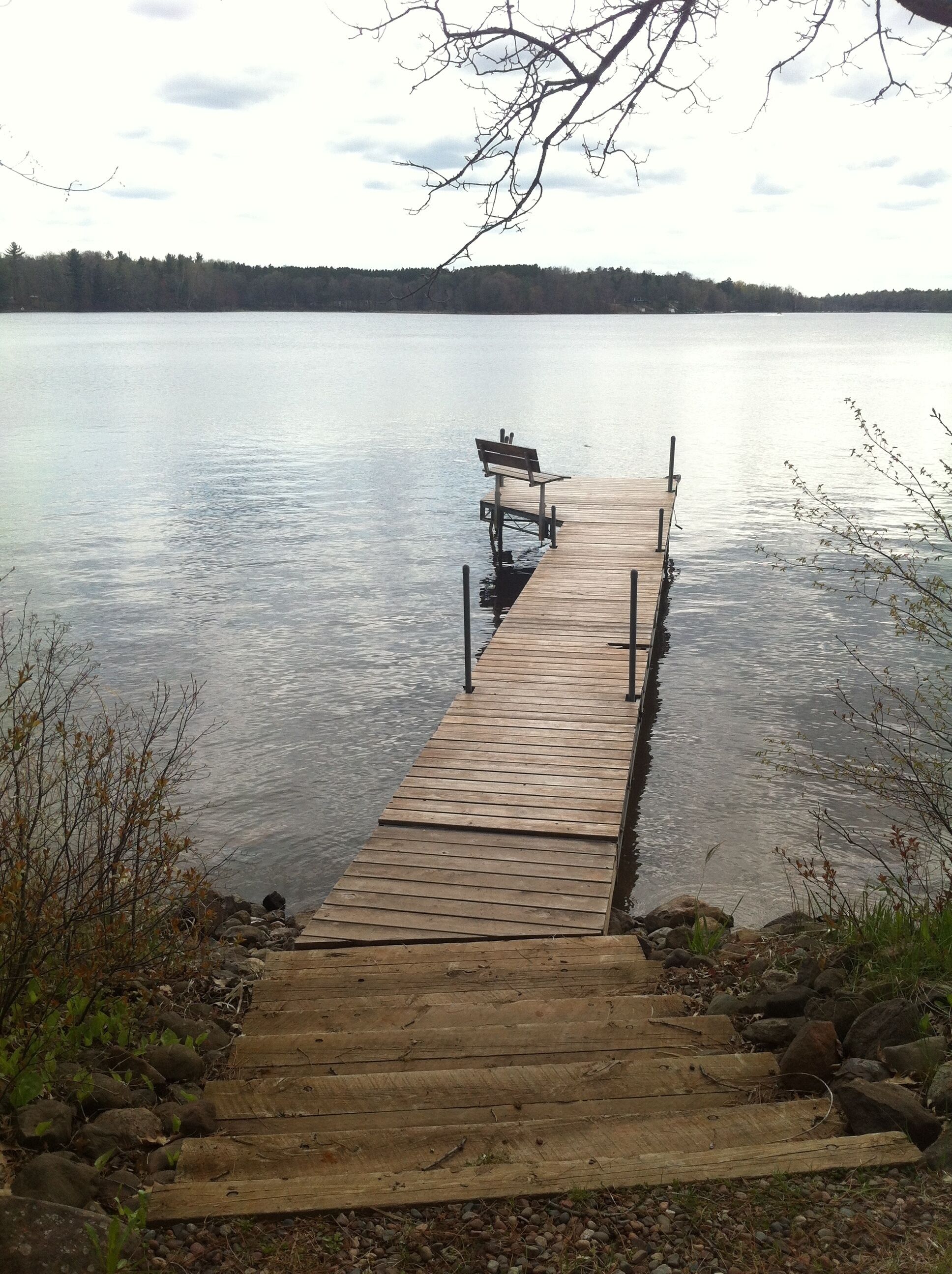 A wooden dock extending into calm water with a bench at the end.