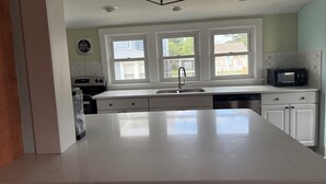 Cozinha com bancadas brancas, micro-ondas embutido, pia e janela com vista para o exterior.