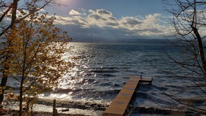 A wooden pier extending into a calm sea, surrounded by trees with autumn leaves.