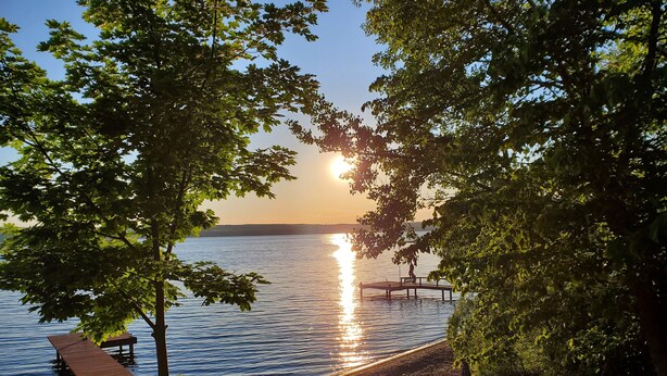 A lakeside deck with wooden benches and a picnic table, surrounded by trees.