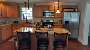 A kitchen with wooden cabinets, a stainless steel refrigerator, a microwave, and a large island with bar stools.