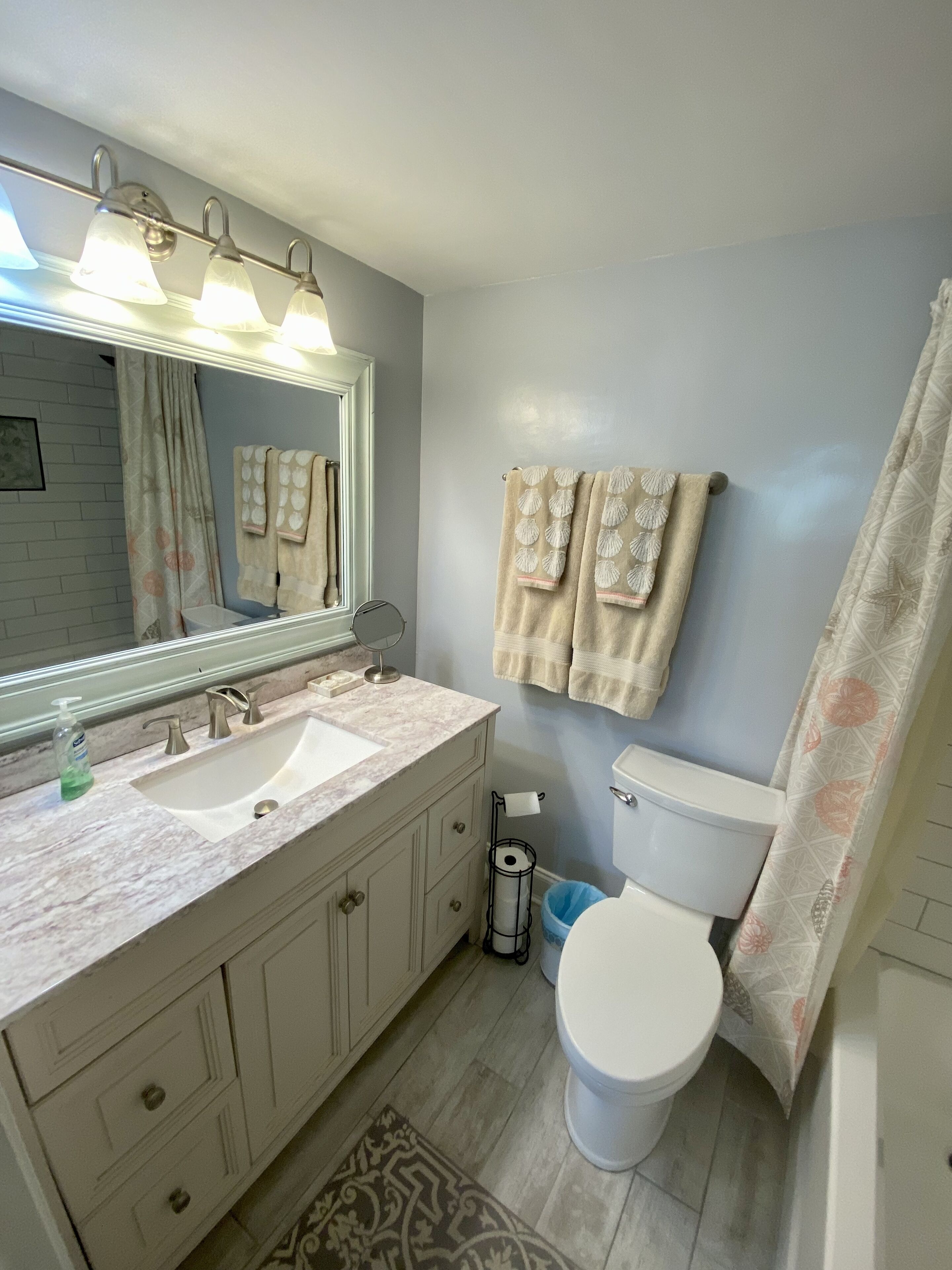 Un baño con lavamanos doble, inodoro, cortina de ducha y espejo con luces.