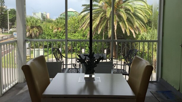 Un balcón con mesa y sillas, con vistas a un jardín exuberante con palmeras y un edificio al fondo.