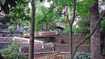 A multi-level outdoor staircase surrounded by dense foliage, with a brick wall and metal railings.