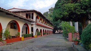 A building with a red and white facade, multiple arches, and a cobblestone pathway. - Hotel Los Cedros (Uruapan)