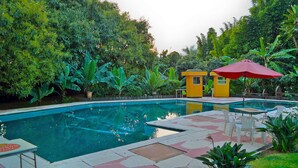 A swimming pool with a tiled deck, surrounded by lush greenery and a small yellow structure. - Hotel Los Cedros (Uruapan)