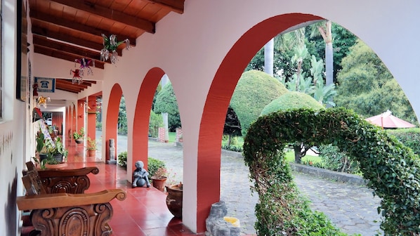 A covered walkway with red arches, potted plants, and a statue. - Hotel Los Cedros (Uruapan)