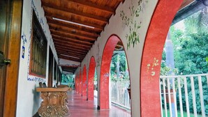 A covered corridor with wooden beams and red pillars, leading to a garden area. - Hotel Los Cedros (Uruapan)