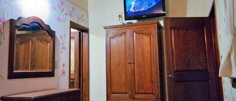 A room with a wooden wardrobe, a mirror, a television on a stand, and a small table.