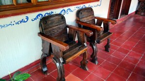 Two wooden chairs with armrests, a tiled floor, and a wall with blue decorative writing. - Hotel Los Cedros (Uruapan)