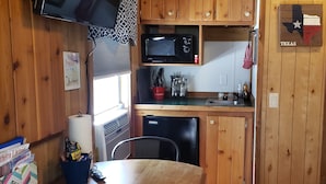 A compact kitchen with wooden cabinets, a microwave, a sink, and a small refrigerator. - The Roadrunner Tiny Cabin at Palo Duro  (Canyon)