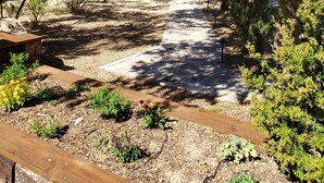 A paved pathway leading through a wooded area with benches and a small garden. - The Roadrunner Tiny Cabin at Palo Duro  (Canyon)