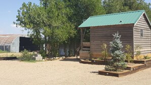 A rustic wooden cabin with a green roof, surrounded by gravel and small plants. - The Roadrunner Tiny Cabin at Palo Duro  (Canyon)