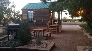 Un chalet rustique avec une façade en bois, un petit porche, un barbecue et un chemin de pierre menant à l’entrée.