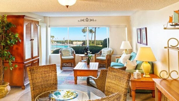 A spacious living room with wicker furniture, a glass coffee table, and a view of the ocean through large windows.
