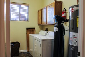 A laundry room with two washers and a dryer, a water heater, and wooden cabinets above.