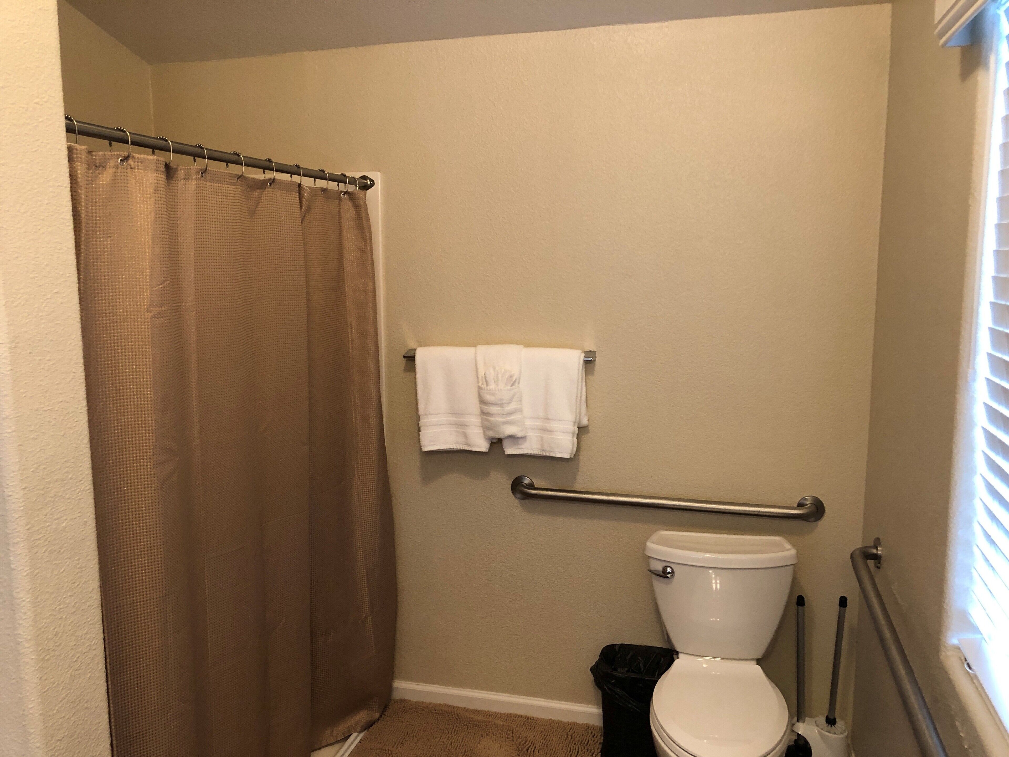 A bathroom with a shower curtain, a toilet, a grab bar, and a towel rack.