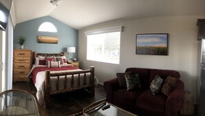 A bedroom with a bed, a wooden dresser, a red sofa, a window with blinds, and a refrigerator. - Deluxe "Sunset" Vacation rental in private marina on the California Delta (Stockton)