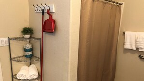 A bathroom with a shower curtain, a metal shelf with towels, a broom, and a small potted plant. - Deluxe "Sunset" Vacation rental in private marina on the California Delta (Stockton)