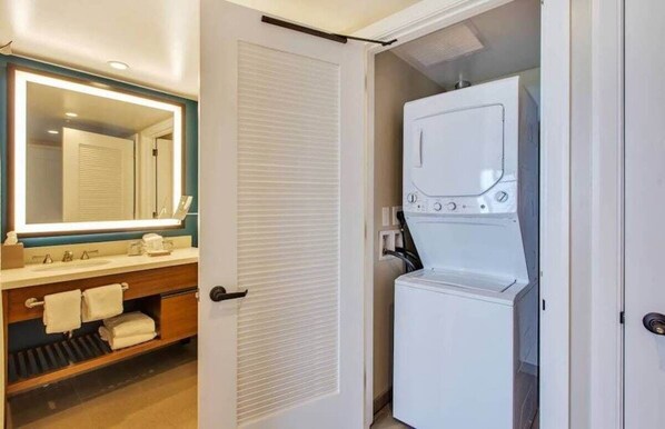 A compact bathroom with a built-in washing machine, a mirror, and a vanity with towels. - Westin Nanea in Maui Available December 23-Dec 30, 2024 (Lahaina)