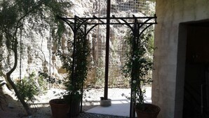 Un patio con pérgola, plantas en macetas y un muro de piedra.