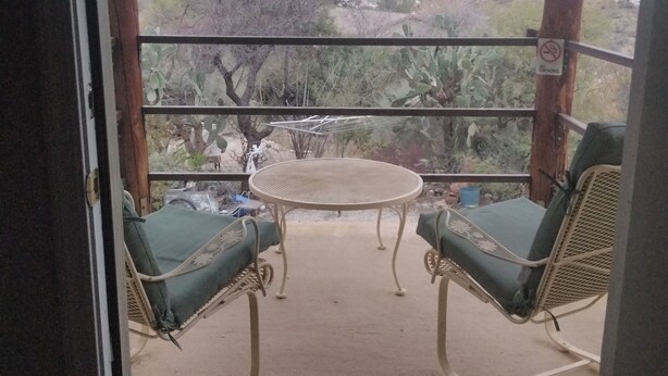 Un balcón con una mesa y dos sillas, con vistas a un paisaje desértico y montañas al fondo.