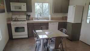 Cocina con estufa, microondas, fregadero y refrigerador. Hay una mesa con sillas y una ventana sobre el fregadero.