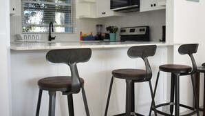 A kitchen with white cabinets, a black microwave, and three bar stools with dark seats.