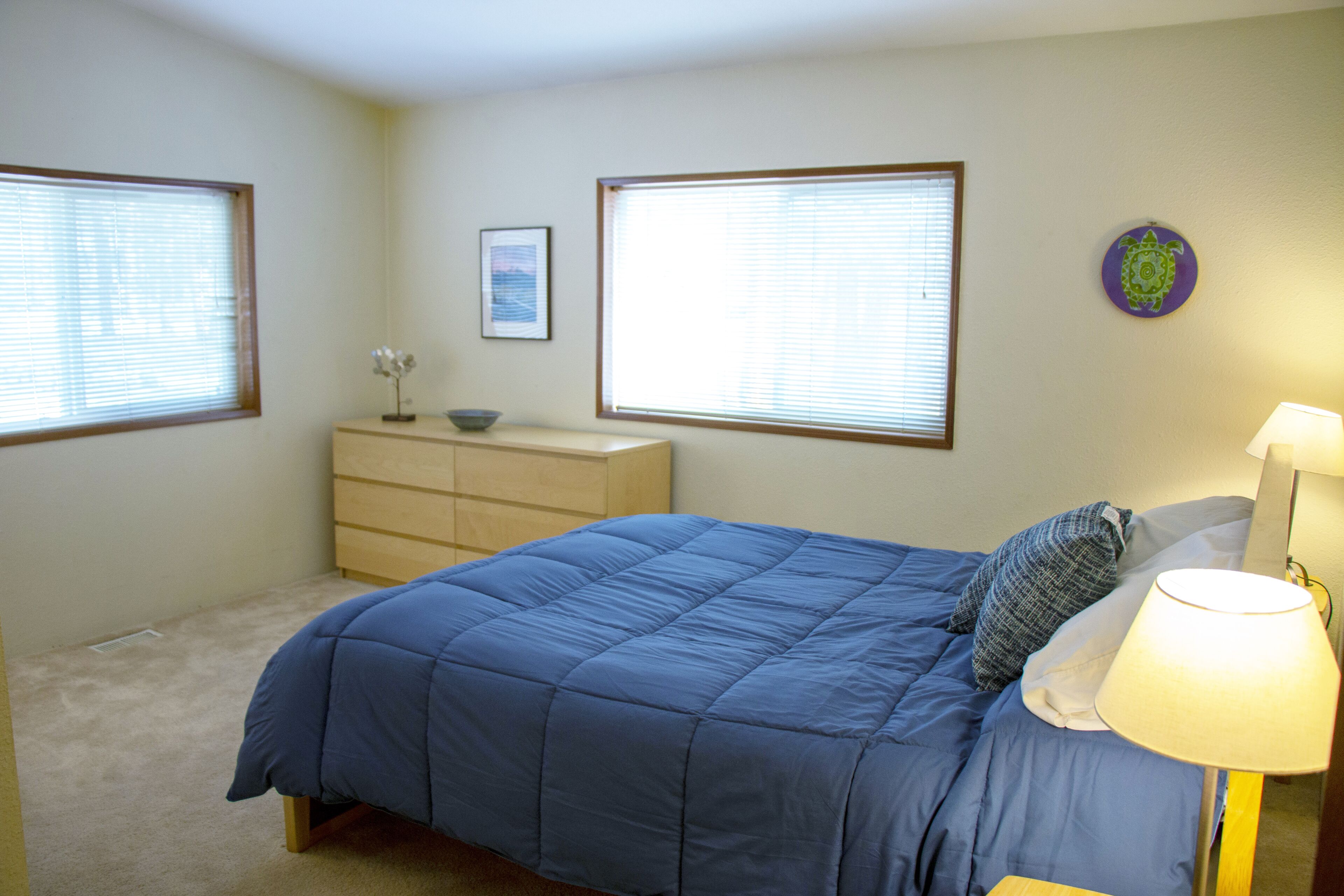 Une chambre à coucher avec un lit, une commode, des fenêtres et un élément décoratif mural.