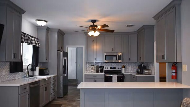 A modern kitchen with grey cabinets, a central island, a ceiling fan, and a microwave. - Happy Valley retreat - whole house, large living room, EV charger (Port Matilda)
